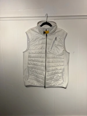 Parajumpers Zavier Hybrid Vest vit  - Snygg vit dunväst med quiltat mönster och hög krage. Västen har dragkedja framtill, bröstficka med dragkedja och två sidofickor. Perfekt för lager-på-lager och passar till många olika stilar. Storlek L men sitter bra på en M