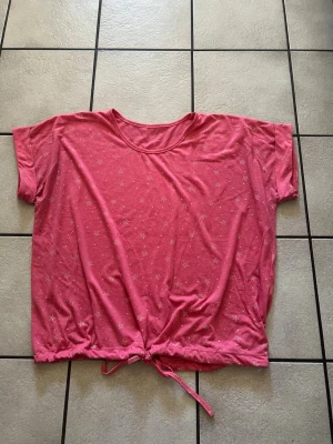 Rosa croppad topp med knyt storlek XL - Säljer en rosa croppad topp med små vita stjärnor som mönster. Toppen har korta ärmar och ett knytband i nederkanten för en snygg passform. Perfekt för dig som gillar en avslappnad men trendig stil.