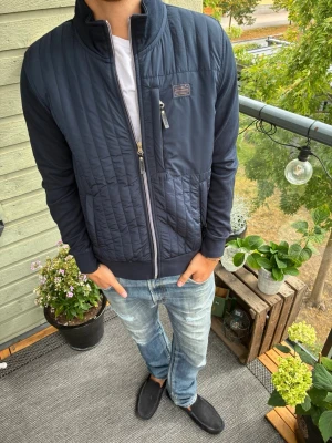 Mörkblå cardiganjacka från Signal - Snygg mörkblå jacka från Signal med hel dragkedja framtill och hög krage. Jackan har en bröstficka med dragkedja och ribbade muddar vid ärmslut och nederkant. Perfekt för dig som gillar stilren och enkel design.