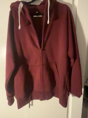 Vinröd hoodie Russedress - Säljer en vinröd hoodie från Russedmerch med dragkedja framtill, vita snören i huvan och fickor på sidorna. Mjuk och skön bomullsblandning, perfekt för chill dagar. Stort tryck med Russedress-logga på ärmen.