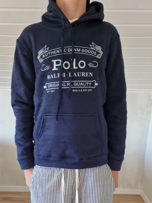 Polo Ralph Lauren zip hoodie - Snygg marinblå hoodie från Polo Ralph Lauren med vit logga och text på bröstet. Klassisk huva med dragsko och stor magficka framtill. Perfekt för en avslappnad och trendig stil. Mjuk bomullsblandning som känns skön mot huden.