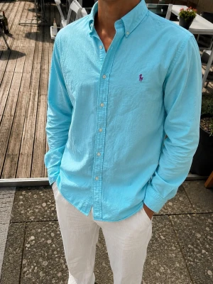 Ralph Lauren Featherweight Twill Skjorta – Turkos/Blå – Stl S - Snygg Ralph Lauren skjorta i en ljus turkos/blå färg med klassisk lila Polo-logga på bröstet. Tillverkad i 100 % bomull och i Ralph Laurens tunna och lätta Featherweight Twill-kvalitet. Button-down-krage, klassisk passform och pärlemorliknande knappar.  Perfekt till sommaren och passar lika bra till vita linnebyxor som till jeans eller shorts. Skjortan är i fint skick och har en naturligt lätt, ledig struktur.  Material: 100 % bomull Modell: Featherweight Twill Storlek: S Färg: Ljus turkos/blå