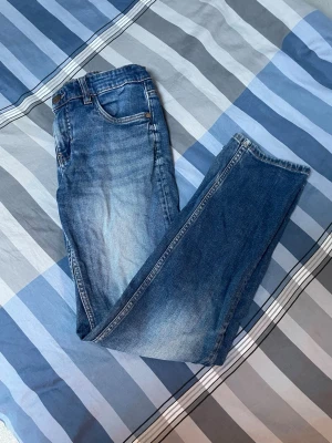 Blå raka jeans med slitningar - Säljer ett par klassiska blå jeans med raka ben och lätt slitna detaljer framtill. Jeansen har fem fickor och normal midja. Perfekta till en avslappnad stil och passar till det mesta. Materialet är denim i bomull.