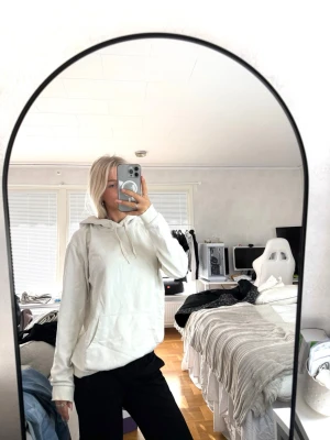 Vit hoodie med huva och ficka - Säljer en enkel och stilren vit hoodie med huva och dragsnören. Hoodien har en stor magficka och ribbade muddar vid ärmslut och nederkant. Perfekt för dig som gillar en clean och avslappnad look. HAR FLÄCKAR vid armarna och insidan av nacken! 