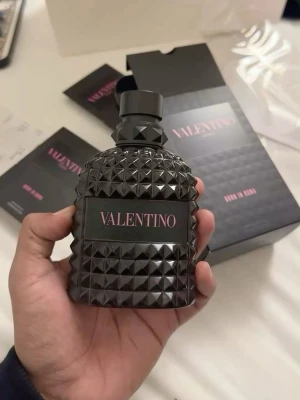 Valentino parfym svart flaska - Snygg parfym från Valentino i en svart, mönstrad flaska med nitar och elegant etikett. Flaskan har en lyxig och modern design som sticker ut på hyllan. Perfekt för dig som gillar exklusiva dofter och coola detaljer.