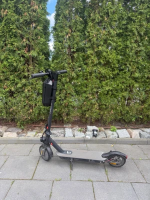 Svart elscooter med förvaringsväska - Säljer en svart elscooter med grått deck och röda detaljer. Scootern har en praktisk svart förvaringsväska monterad på styret och robusta hjul. Perfekt för smidig transport i stan eller till skolan.