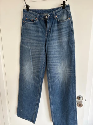 Blå vida jeans från Weekday - Säljer ett par blå jeans från Weekday med rak passform och klassisk femficksdesign. Jeansen har en ljus tvätt med diskreta slitningar och är tillverkade i denim. Perfekta för en avslappnad och trendig stil.