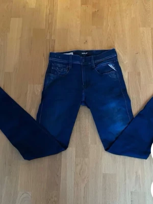 Mörkblå slim fit jeans Replay - Snygga mörkblå slim fit jeans från Replay med klassisk femficksdesign och subtila slitningar framtill. Jeansen har normal midja och smala ben, perfekta för en trendig och avslappnad look. Materialet är stretchigt för extra komfort.