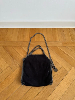 Axelremsväska - Axelremsväska i svart med kedjedetaljer runt kanterna och som axelrem. Höjd: 29 cm. Bredd: 26 cm.