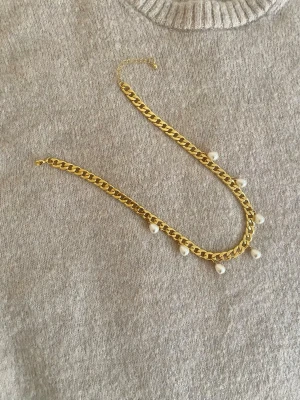 Guldhalsband med pärldetaljer - Snyggt halsband i guldfärgad rostfritt med chunky kedja och små vita pärlor som hänger längs kedjan. Perfekt för att ge en trendig touch till din outfit. Justerbar längd med kedjeförlängning.