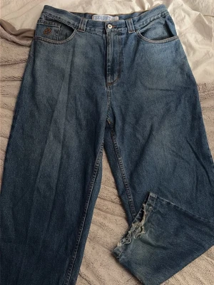 Blå pösiga raka jeans med slitna benslut - Ett par klassiska blå jeans från big boy polar med rak passform och slitna, fransiga och blekta benslut för en avslappnad och trendig look. Jeansen har dragkedja gylf med en knapp. Perfekta för dig som gillar vintagekänsla och streetstyle. 
