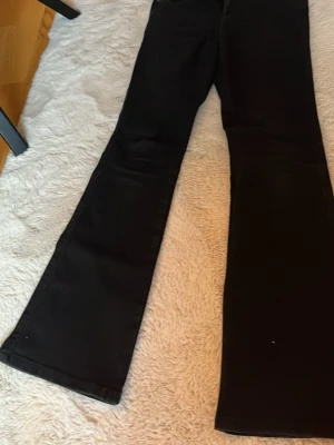 Svarta bootcut jeans - Säljer ett par svarta bootcut jeans med klassisk passform. Jeansen har utsvängda ben och är perfekta för dig som gillar en tidlös och clean stil. Materialet känns mjukt och bekvämt, och färgen är riktigt djup svart.