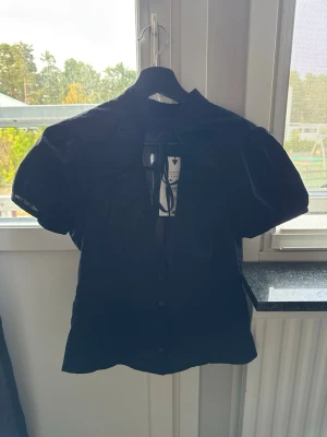 Svart blus med puffärm och knappar - Stilren svart blus med puffiga korta ärmar, säljer den då den inte passade mig och är väldigt tajt i storleken.