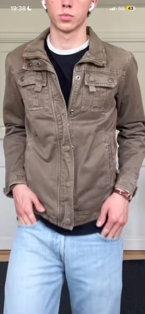 Vintage field jacket - Snygg brun utilityjacka i bomull med klassisk krage, bröstfickor med lock och knappar samt patch på ena ärmen. Jackan har dragkedja och knappstängning framtill och raka ärmar. Perfekt för en avslappnad streetstil. Storlek xs kan passa S också!