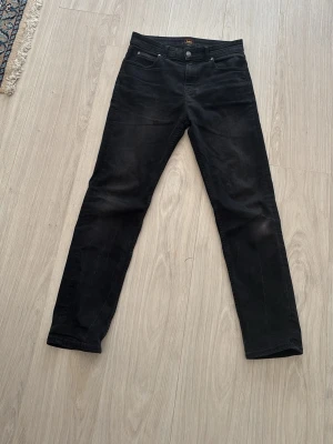 LEE slim fitt jeans - Snygga svarta slim fit jeans från LEE med klassisk femficksdesign och knappgylf. Jeansen har raka ben och är tillverkade i ett stretchigt material som ger en bekväm passform. Perfekta för en stilren och enkel look.