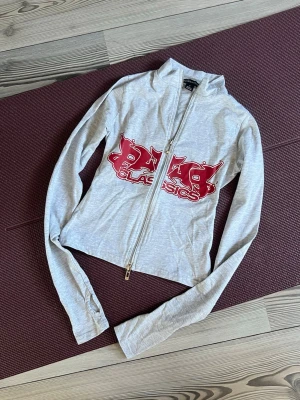 Ljusgrå ziptröja  - Säljer en Snygg ljusgrå ziptröja med röd print! Tröjan är från pretty little things i storlek S. Den är nästan helt oanvänd och i väldigt bra skick!💕