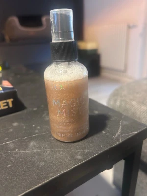 Magic Mist illuminating face mist - Magic Mist illuminating face mist i en genomskinlig plastflaska med svart spraykork. Innehållet är skimrande bronsfärgat och flaskan rymmer 80 ml. Perfekt för att ge huden glow och fräsch finish.