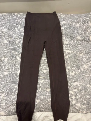 Bruna höga leggings - Säljer ett par bruna leggings med hög midja och lång passform. Materialet är stretchigt och bekvämt, perfekt för att chilla eller träna. Diskret G-logga på ena benet. Snygga och enkla att matcha med olika outfits.