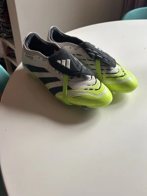 Adidas Predator fotbollsskor vit/neon - Säljer ett par Adidas Predator fotbollsskor i vitt med svarta och neon-gula detaljer. Skorna har klassisk tunga med kardborre och de ikoniska tre ränderna på sidan. Perfekta för dig som vill sticka ut på planen med både stil och funktion.