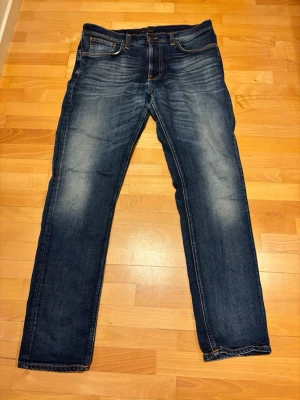 Nudie Jeans Mörkblå - Hej, säljer nu dessa Nudie Jeans i storlek W36, L32! Skit snygg tvätt i ändå väldigt bra skick, enda är ett litet rev/hål som du kan se på bild tre. Pris ej hugget i sten och bara säga till vid frågor!