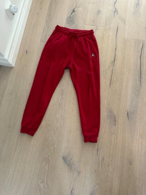 Röda mjukisbyxor med logga - Snygga röda mjukisbyxor från Jordan med resår i midjan. Byxorna har ribbade muddar vid bensluten och en liten Jordan logga på vänster lår. Riktigt sköna byxor som funkar till allt ifrån träning till ren stil.