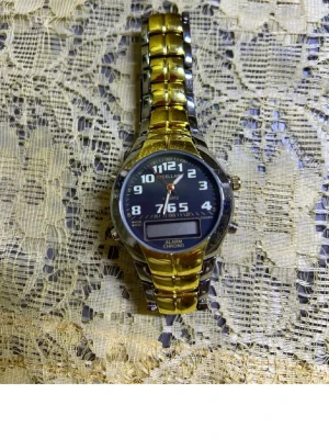Guldig och silverfärgad analog klocka - Snygg klocka med både guld- och silverfärgad länkarmband och svart urtavla. Klockan har tydliga vita siffror, digital display och flera knappar på sidan. Perfekt accessoar för dig som vill sticka ut lite extra. Helt ny 