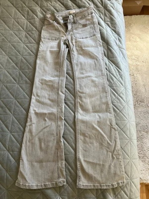 Ljusgråa utsvängda jeans - Säljer ett par ljusgråa jeans med utsvängda ben och hög midja. Klassisk femficksmodell med snygga sömdetaljer och raka bakfickor. Jeansen är i ett mjukt denimtyg som passar perfekt till en trendig vardagslook.