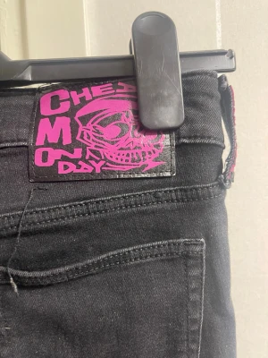 Svarta bootcut jeans Cheap Monday - Säljer ett par svarta jeans från Cheap Monday med bootcut-modell. Jeansen har en cool rosa logga med döskalle på bakfickan och klassisk femficksdesign. Materialet är denim med lite stretch för skön passform. Perfekta för dig som gillar streetstyle och edgy detaljer.
