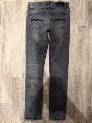 Nudie Jeans Lean Dean Grå W30/L34 - Slim Tapered Fit - Nudie Jeans Lean Dean ”Mono Grey” grå jeans med slim tapered-passform, normalhög midja och avsmalnande ben, storlek W30/L34, midja 40 cm, ytterbenslängd 112,5 cm, benöppning 15,5 cm, modellen är 185cm & väger 65kg, i fint skick.