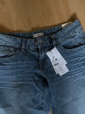 Blå wide jeans med låg midja - Säljer ett par klassiska blå jeans med wide modell  och låg midja. Jeansen har fem fickor, bälteshällor och stängs med knapp och dragkedja. Materialet är denim i 100% bomull och färgen är en snygg tvättad blå nyans.