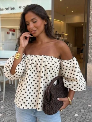 Prickig offshoulder blus med puffärm - Trendig offshoulder blus i vitt med svarta prickar och puffiga trekvartsärmar. Luftig och snygg modell som ger en cool vibe till din outfit. Perfekt att matcha med jeans eller kjol för en stilsäker look.