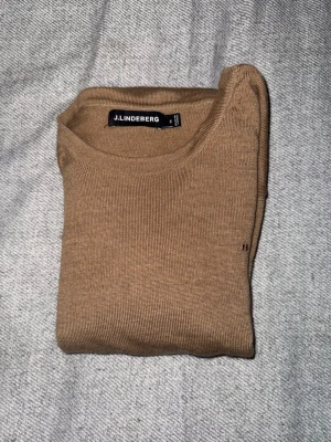 Beige stickad tröja J.Lindeberg - Beige stickad tröja från J.Lindeberg i 100% merinoull. Tröjan har rund halsringning samt ribbade muddar vid ärmslut och nederkant. Kan gå ner i pris