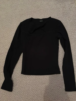 Svart långärmad topp - En enkel och stilren svart långärmad topp med rund hals. Toppen har en tight passform och är perfekt att matcha med olika outfits. Materialet känns mjukt och stretchigt, vilket gör den bekväm att bära. Väldigt cool knut där framme vilket gör den unik, bra fest topp.
