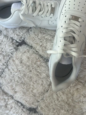 Helvita klassiska sneakers - Säljer ett par helvita sneakers med lågt skaft och perforerade detaljer på tån. Skorna har en stilren design med vita snören och sula. Tillverkade i slätt läderliknande material och passar perfekt till streetwear eller casual outfits.