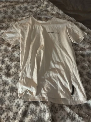 Vit basic t-shirt med tryck - En vit t-shirt i klassisk modell med korta ärmar och rund hals. T-shirten har ett diskret tryck på bröstet och är tillverkad i mjukt bomullsmaterial. Perfekt för en avslappnad och stilren look.