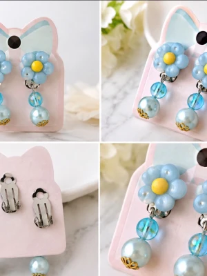 Blå blomörhängen med pärlor - Söta örhängen i form av blå blommor med gul mitt, dekorerade med blå pärlor och transparenta kulor. Örhängena har clipsfäste och detaljer i silverfärgad metall. Perfekta för att ge en lekfull touch till din stil.