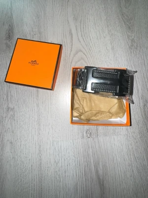Svart bälte med stor spänne - Snyggt svart bälte från  med det ikoniska spännet i metall. Kommer i original orange box. Perfekt accessoar för att lyfta vilken outfit som helst. Klassisk design och exklusiv känsla.