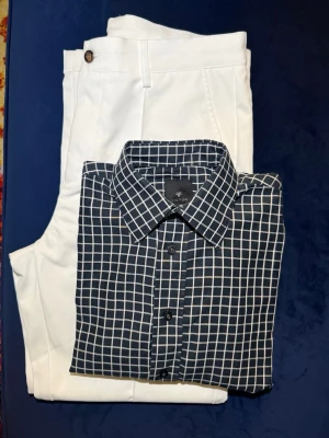 Svart rutig skjorta med vit ruta - Stilren svart skjorta med vitt rutmönster och klassisk krage. Skjortan har lång ärm och knäppning framtill. Perfekt för dig som gillar en clean och modern look. Tillverkad i mjukt bomullsmaterial som känns skönt mot huden.