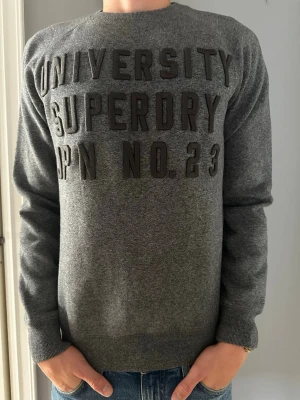 Grå Superdry Sweater  - Tja den är i mycket bra skick o storlek S från Superdry. Modellen brukar bära M/S och är 180cm lång. Vid funderingar om mått är det bara att skicka, pris ej hugget i sten. Inga defekter.