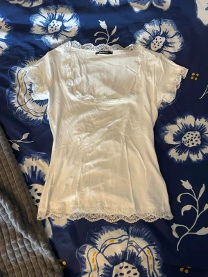 Vit spets topp  - Supersöt vit topp från Gina Tricot med spetsdetaljer runt halsringning, ärmslut och nederkant. Modellen har korta ärmar och en fyrkantig urringning. Tunn och mjuk i materialet, perfekt för lager på lager eller sommaroutfits.