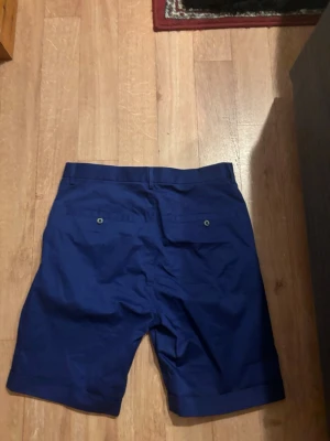 J.lindberg golf shorts - Snygga mörkblåa golf shorts uppvikta benslut och två bakfickor med knapp. Klassisk passform och bälteshällor i midjan. Perfekta för sommaren och såklart till golf. Priset är så klart inte hugget i sten om det är några flera frågor är det bara att höra av sig😃