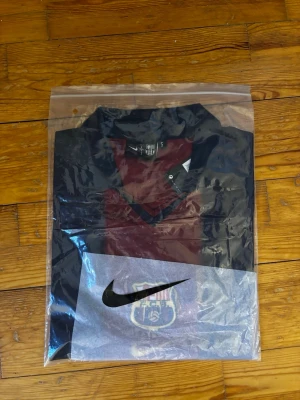 Barça tröja från Nike, vinröd/blå - Säljer en FC Barcelona tröja från Nike i vinrött och mörkblått. Tröjan har V-ringning och klubbens emblem på bröstet. Perfekt för dig som älskar fotboll och vill visa ditt stöd för laget.