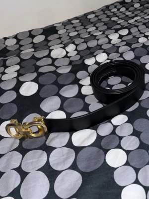 Svart Ferragamo läderbälte - Snyggt svart bälte från Ferragamo i äkta läder med en ikonisk guldfärgad dubbel-Gancio-spänne. Perfekt accessoar för att lyfta vilken outfit som helst och ger en lyxig touch till din stil.