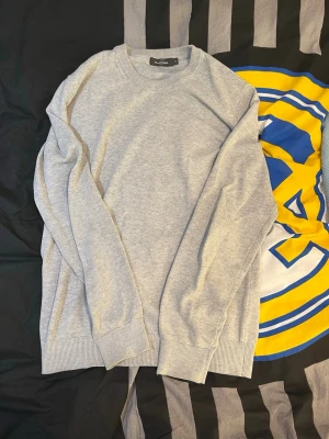 Stickad tröja - En stilren ljusgrå tröja från dressman med rund halsringning och ribbade muddar vid ärmslut och nederkant. Perfekt för lager på lager och enkel att matcha med olika outfits. Tillverkad i mjukt material för skön komfort.