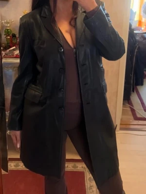 Klassisk lång skinnkappa Hollies - Superfin och tidlös lång skinnkappa / läderrock från det svenska kvalitetsmärket Hollies Leather. Modellen är figursydd med en snygg siluett, klassisk krage med slag och stängs med fyra knappar framtill. Den har eleganta fickdetaljer både på bröstet och i midjan.Perfekt vintage / 90-talslook som passar till allt! Lädret är av hög kvalitet och i mycket gott skick.