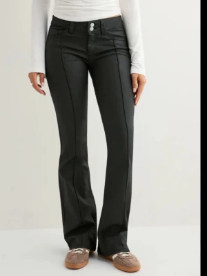 Svarta bootcut skinnbyxor med pressveck - Snygga svarta bootcut jeans/skinnbyxor med pressveck framtill och dubbla knappar i midjan. Byxorna  har klassiska fickor fram och bak samt markerade sömmar. Dem är köpta på Nelly för 700kr