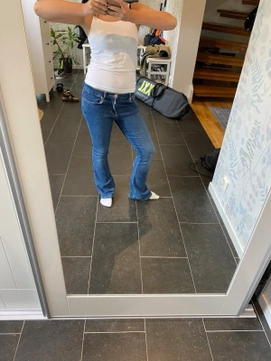 Blå bootcut jeans med snörning - Säljer ett par blå bootcut jeans med snygg snörning i midjan som är perfekta nu till hösten! Jeansen har en klassisk femficksmodell och sitter tajt över låren för att sedan bli vidare nedtill. Perfekta för dig som gillar en retro och avslappnad stil. 