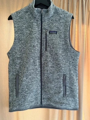 Grå fleecväst från Patagonia - Snygg  fleecväst från Patagonia (stonewash) med hög krage och hel dragkedja. Skön och varm perfekt till hösten. Storlek M sitter slim mot kroppen. Använd 2 gånger helt i nytt skick. 