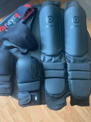 Svart kampsports skyddspaket Chokem - Ni kan köpa varorna var för sig också. Säljer ett komplett svart skyddspaket från Chokem för kampsport. Paketet innehåller benskydd, handskar och suspensoar. Alla delar är vadderade och har justerbara kardborreband för bästa passform. Perfekt för träning inom MMA, thaiboxning eller liknande. 
