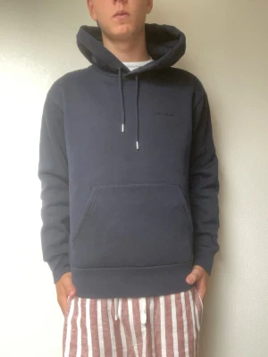 J.Lindeberg Hoodie (mörkblå, pullover) - Säljer en stilren mörkblå hoodie från J.Lindeberg. Bekväm modell med broderad logga ton-i-ton på bröstet, känguruficka och justerbar huva. Perfekt till både vardag och avslappnade outfits.  * Skick: Mycket bra * Färg: Mörkblå * Passform: Normal * Modell på bild: 178 cm / 70 kg  Hör gärna av dig vid frågor eller om du vill ha fler bilder!